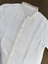 Camisa blanca de lino con cuello mao y detalle de puntilla de algodón en cuello y cartera de botones. Cierre frontal con botones de nácar.