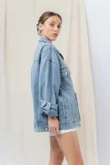 Campera denim celeste de corte oversize, con cuello clásico, cierre frontal con botones metálicos, bolsillos delanteros con solapa, bolsillos laterales y mangas largas con puños abotonados.