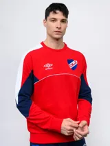 Buzo de felpa azul marino, con mangas largas, cuello redondo y puños acanalados. Presenta cortes en blanco y rojo en la parte superior, logo de Umbro bordado en el pecho y escudo del Club Nacional de Football.