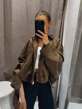 Bomber jacket color marrón de gamuza sintética, con cuello camisero, hombros caídos y elástico en la cintura.