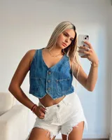 Chaleco de jean azul claro, estilo crop top, con cuello en V, cierre frontal de botones y dos bolsillos pequeños en el pecho.