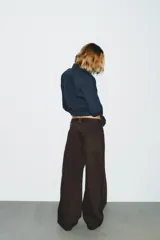 Jeans de mezclilla color marrón oscuro, tiro bajo, corte baggy barrel (ancho y holgado con caída recta). Presenta cinco bolsillos y cierre frontal con cremallera y botón metálico.