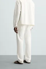 Pantalón de jean color blanco, corte recto, con bolsillos frontales y traseros, y cierre frontal con cremallera y botón.