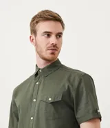 Camisa de hombre de manga corta en lino color blanco, con cuello clásico, botonadura frontal y bolsillo de parche en el pecho. Corte recto.