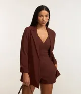 Blazer sastre femenino confeccionado en crepé color marrón, de modelo oversized y comprimento alargado. Sin estampa, posee bolsillos y detalle de pliegues en los puños.