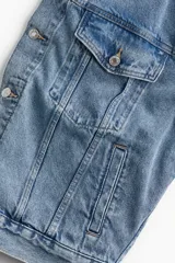 Campera de jean azul claro, corte oversized, con cuello clásico, cierre frontal con botones metálicos, bolsillos con solapa abotonada en el pecho y bolsillos laterales.