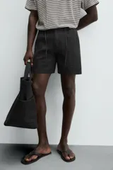 Bermuda negra regular fit confeccionada en tejido con mezcla de algodón y lino. Cintura elástica ajustable con cordón. Pliegues frontales. Bolsillos laterales y traseros de vivo. Cierre frontal con cremallera y botón.