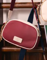 Bandolera de cuerina bicolor, roja y beige, con correa regulable y tag frontal con logo 'The Brunch Club'.