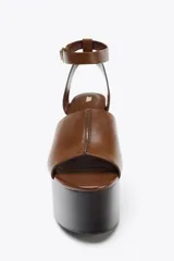Sandalias de cuero color marrón con plataforma de cuña de madera oscura y correa de tobillo ajustable con hebilla dorada.