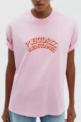 Camiseta rosa de algodón con efecto lavado, corte regular, cuello redondo y mangas cortas. Estampado frontal con la frase "Puerto Rico Vuela Conmigo".