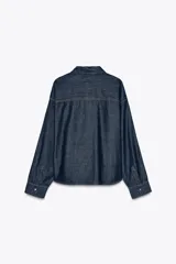 Camisa de denim azul oscuro, corte amplio, cuello solapa, manga larga y cierre frontal con botones a presión.