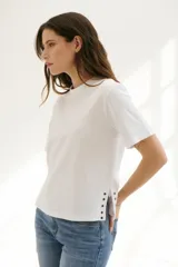 Remera blanca de algodón de corte recto, con cuello redondo y mangas cortas. Presenta detalle de aberturas laterales con ojales metálicos.