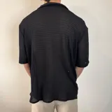 Camisa negra de tejido calado con cuello solapa, manga corta y cierre frontal con botones.
