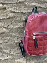 Mochila color bordó con textura tipo cuero de reptil en la parte superior y diseño capitoneado en la parte inferior. Tiene un bolsillo frontal con cierre y tiras regulables.