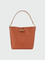 Bolso tipo hobo de cuero color terracota, con cierre metálico dorado y correa de hombro ajustable.