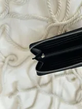 Billetera grande de cuero negro con cierre metálico y logo grabado.