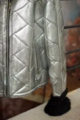 Chaqueta de cuero plateada con acabado metalizado y diseño acolchado. Presenta cuello y puños de piel en color negro, cierre frontal metálico y bolsillos laterales con cremallera.