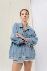 Campera denim celeste de corte oversize, con cuello clásico, cierre frontal con botones metálicos, bolsillos delanteros con solapa, bolsillos laterales y mangas largas con puños abotonados.