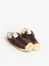 Zapatillas bajas marrones de gamuza con cordones negros, suela color crema con línea celeste y detalle de estrella calada en el lateral.