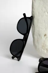 Lentes de sol negros con montura redonda y detalles geométricos en las esquinas superiores.