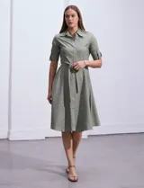Vestido camisero blanco de algodón con cuello con solapa, delantera abotonada, mangas 3/4 regulables con presilla y botón, y cintura con lazo de ajuste.