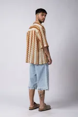 Camisa de manga corta con diseño de crochet a rayas verticales en tonos beige y marrón. Tiene cuello camisero y cierre con botones.