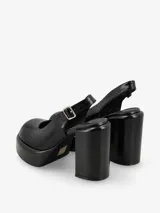 Zapato de tacón negro de charol, con punta redonda, plataforma delantera y correa con hebilla en el tobillo.