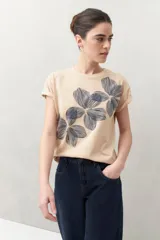 Remera blanca de manga corta con estampado floral en tonos dorados en el frente.