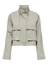 Chaqueta corta color gris claro, con cuello alto ajustable con cordones, cierre frontal con cremallera, bolsillos laterales con solapa y mangas largas. Diseño funcional y moderno.