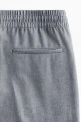 Pantalón gris de sarga con cintura elástica fruncida y cordón ajustable. Piernas amplias con pliegues cosidos, bolsillos laterales discretos y bolsillos decorativos atrás.