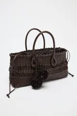Bolso de mano marrón con cuerpo trenzado y doble asa. Incluye charm extraíble y bolsa interior con cierre fruncido.