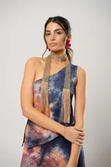 Conjunto de falda larga y top asimétrico con estampado tie-dye en tonos azul, naranja y marrón. El top es de un solo hombro y tiene un collarín con flecos dorados.