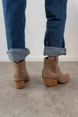 Bota corta de gamuza color marrón oscuro, con puntera cuadrada y detalles de costuras decorativas. Tiene un taco de madera con forma cónica.