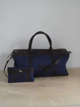 Bolso de lona azul con detalles en cuero marrón, con doble asa de mano y correa de hombro ajustable. Incluye un neceser haciendo juego con logo de caballo bordado.