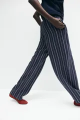 Pantalón de corte holgado en tejido liviano de mezcla de lino a rayas verticales blancas y azul marino. Modelo de tiro alto con cintura elástica y cordón para ajustar fino, bolsillos laterales discretos y piernas rectas.