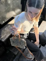 Cartera bandolera pequeña de cuero con estampado animal print, forro de tela y correa larga de cuero marrón.