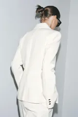 Blazer color blanco confeccionado en algodón, con cuello solapa de muescas y manga larga. Tiene bolsillos con solapa en delantero, forro interior a tono y cierre frontal con botones metálicos en relieve.