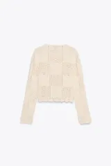 Chaqueta color crudo de tejido de punto calado, con cuello redondo, manga larga y cierre frontal con botones.