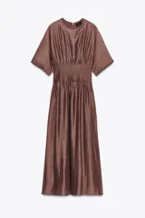 Vestido midi color marrón con textura brillante y arrugada, cuello redondo y mangas cortas tipo murciélago. Presenta un canesú fruncido con pliegues verticales en la cintura que da paso a una falda de corte A.