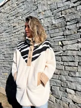 Buzo de polar color crudo con cuello alto, cierre parcial con botones a presión y mangas largas con puños de color beige. Presenta un canesú con estampado de cebra en blanco y negro.
