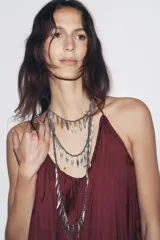 Collar triple plateado con cadenas de eslabones y abalorios metálicos, con colgantes de piezas labradas en forma de hojas.