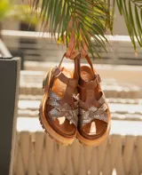 Sandalias bajas de cuero vacuno color beige con tiras cruzadas plateadas y hebilla lateral. Suela doble de goma deportiva con altura de 3cm adelante y 5,5cm atrás.