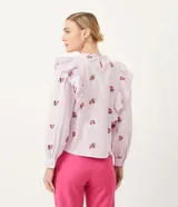 Blusa de algodón a rayas verticales blancas y lilas, con bordado de rosas rosadas. Tiene cuello redondo con volados, mangas largas y volados en los hombros.