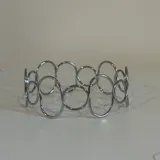 Brazalete de metal con diseño de formas onduladas y acabado brillante.