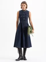 Vestido largo de denim azul oscuro, sin mangas, con cuello mao y cierre frontal de botones. Presenta dos bolsillos con solapa en el pecho y costuras decorativas. La falda es acampanada.