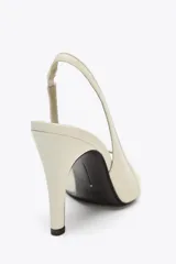 Zapato de tacón color crema, con puntera abierta y tira trasera ajustable.