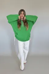 Canguro verde con capucha y cordones blancos, de corte oversize y mangas largas con puños elásticos.