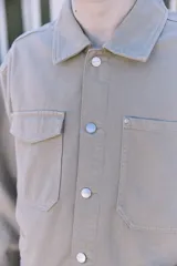 Campera de denim color beige, con cuello amplio, puños con botones y cierre frontal con botones. Incluye bolsillos en el pecho y laterales. Tejido denim de sarga resistente y con protección contra el viento.