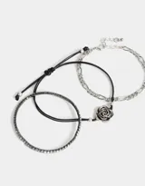 Set de tres pulseras flexibles plateadas: una con strass, una de cadena de eslabones y una con dije de flor metálica.