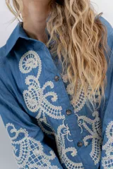 Camisa de denim azul con bordados en color crudo, de corte relaxed, manga larga y botones frontales.